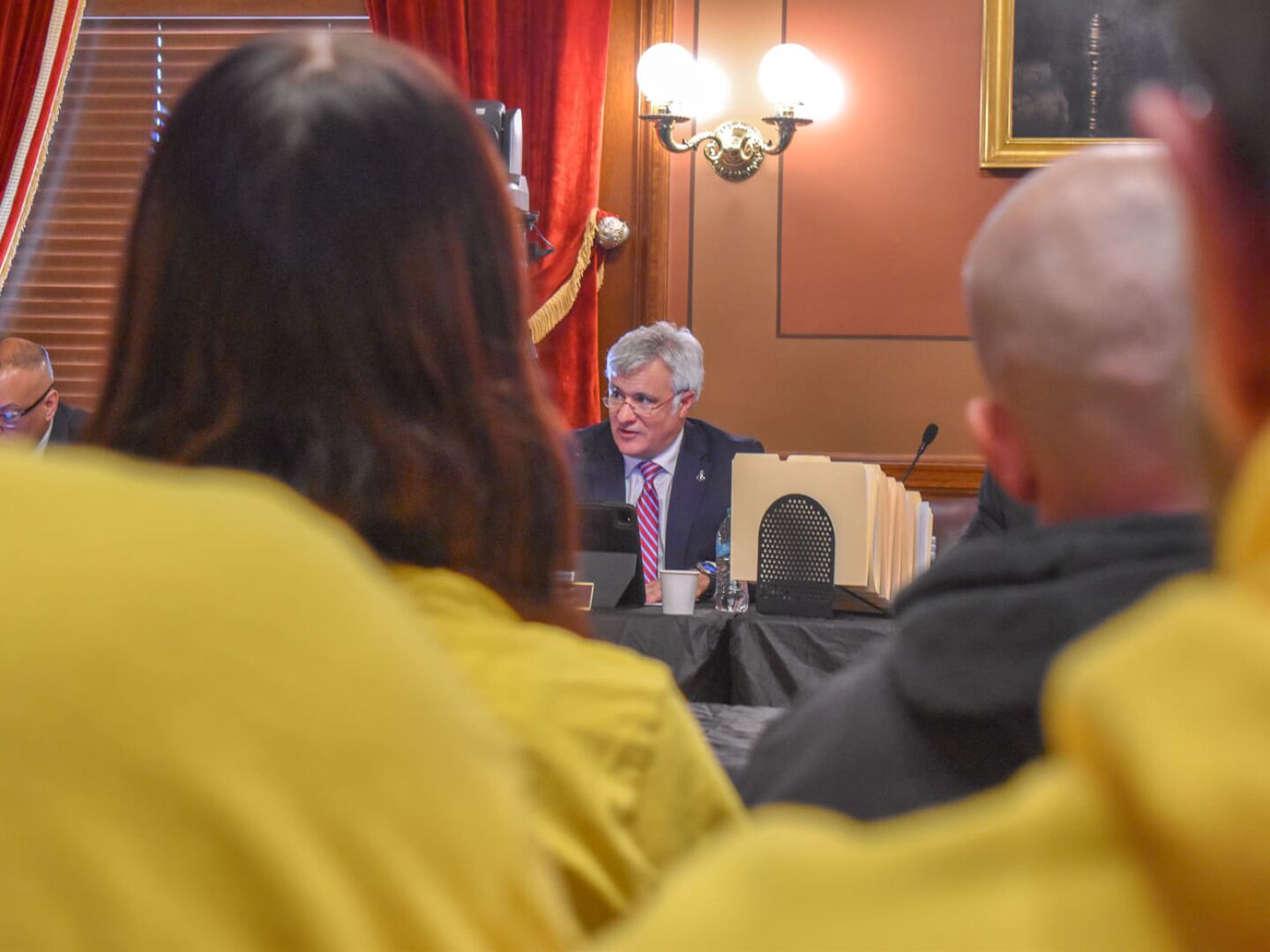 Yellow shirts of Second Amendment supporters frame the view of Rep. Jason Knight, a Barrington Democrat, lead sponsor of the bill to ban assault-style weapons, during a House Committee on Judiciary on Wednesday, March 26, 2025. Knight’s amended bill is set for a vote on Tuesday, June 3.