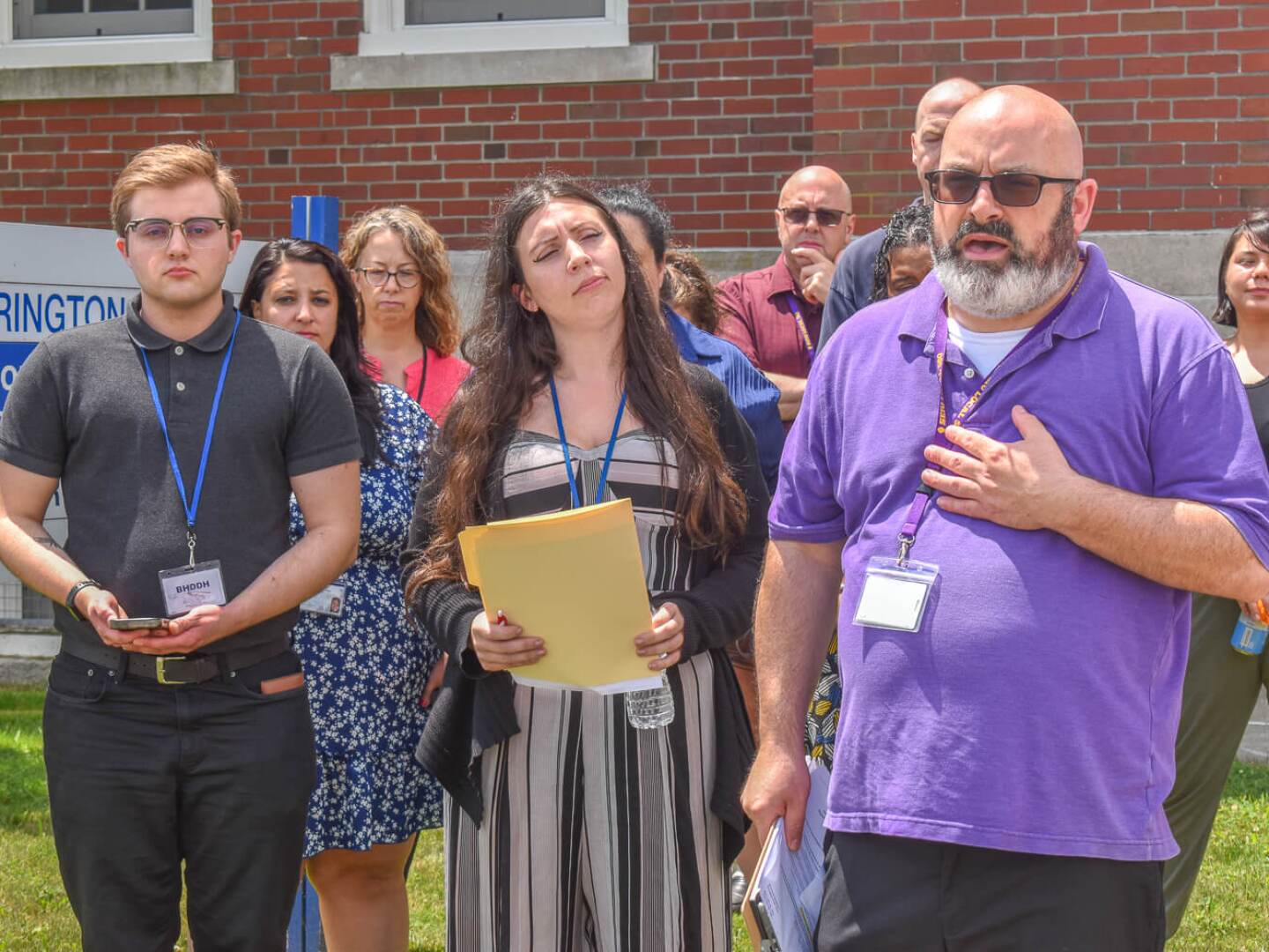 SEIU Local 580 President Matthew Gunnip, right, speaks at a press conference outside the Rhode Island Department of Behavioral Healthcare, Developmental Disabilities and Hospitals (BHDDH) brick office building in Cranston on July 1, 2025. He was joined by disability case managers who are calling on the state to raise their salaries and hire additional workers, including Alex Blue, far left, and Erica MacDougall, center front.