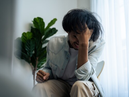 Asian young upset depressed man sitting alone in living room at home. Attractive unhappy male feeling very sad, lonely and frustrated with life problem think of money debt, budget loss, bankruptcy.