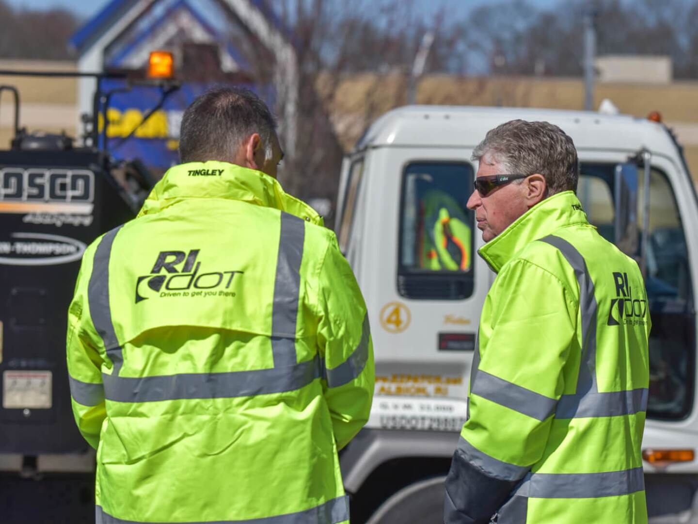 Gov. Dan McKee, right, speaks with interim Rhode Island Department of Transportation Director Robert Rocchio during the state’s launch of its new 5-1-1 service on April 8, 2025. In the background is the ‘Pothole Killer’ contracted by the state to help transportation officials fill road craters.
