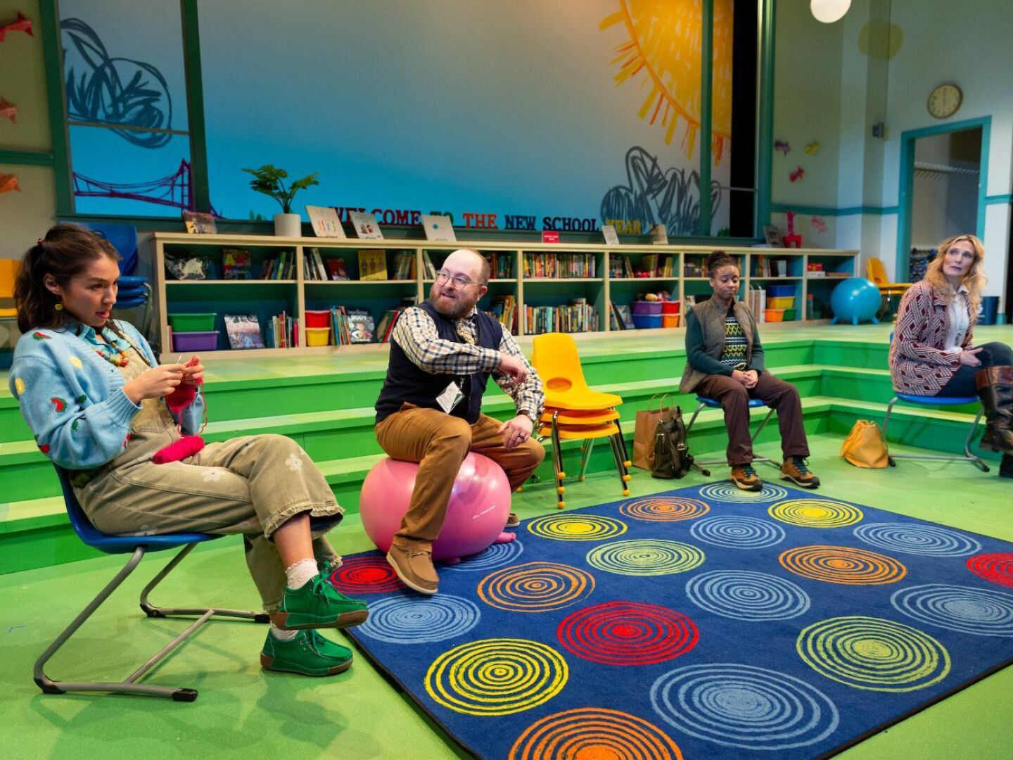 Four performers on a stage set designed to look like an elementary school library.