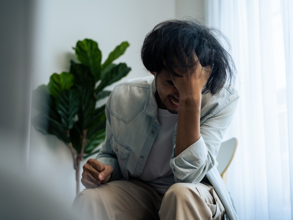 Asian young upset depressed man sitting alone in living room at home. Attractive unhappy male feeling very sad, lonely and frustrated with life problem think of money debt, budget loss, bankruptcy.