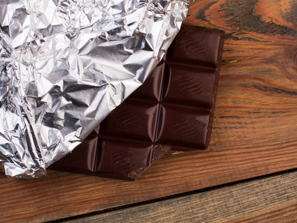Close up of chocolate bar wrapped in silver foil. Dark chocolate bar on rustic wooden background.