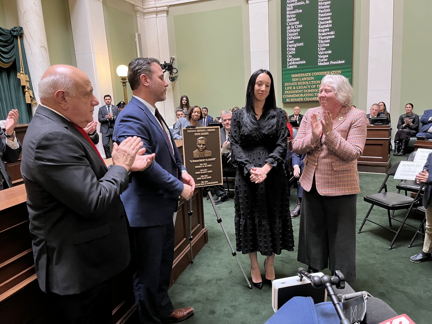 Ruggerio’s children, Charles Ruggerio and Amanda Fallon, flank the plaque dedicated to their father, surrounded by Senate Majority Leader Frank Ciccone (left) and Senate President Val Lawson (right).