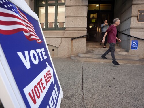 People walk past a sign that points the direction toward a voting location during early voting in the general election, Friday, Nov. 1, 2024, at City Hall in Providence, R.I. (AP Photo/Steven Senne)